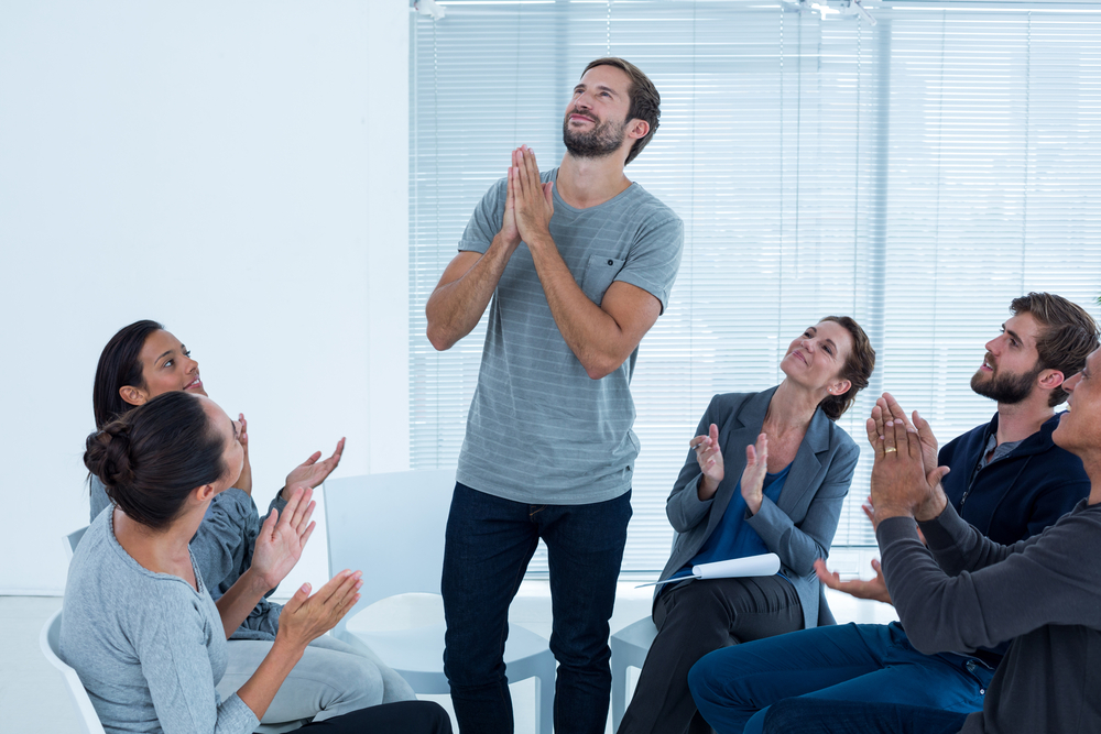 The rehab group applauds a delighted man standing up during a rehab therapy session.