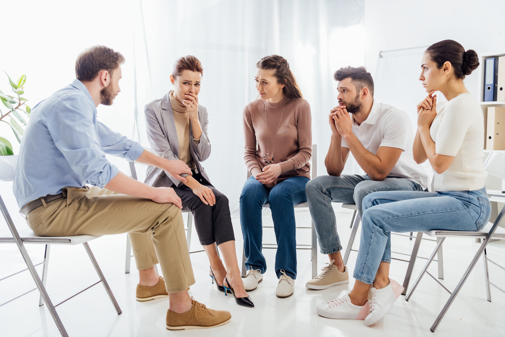 Five individuals are participating in group rehab therapy and discussing their problems.