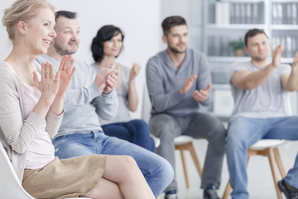 Happy people clapping at support group meeting during rehab group
