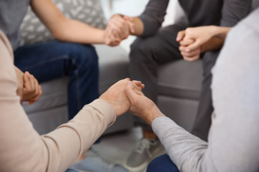 Young people holding hands during rehab group therapy, closeup