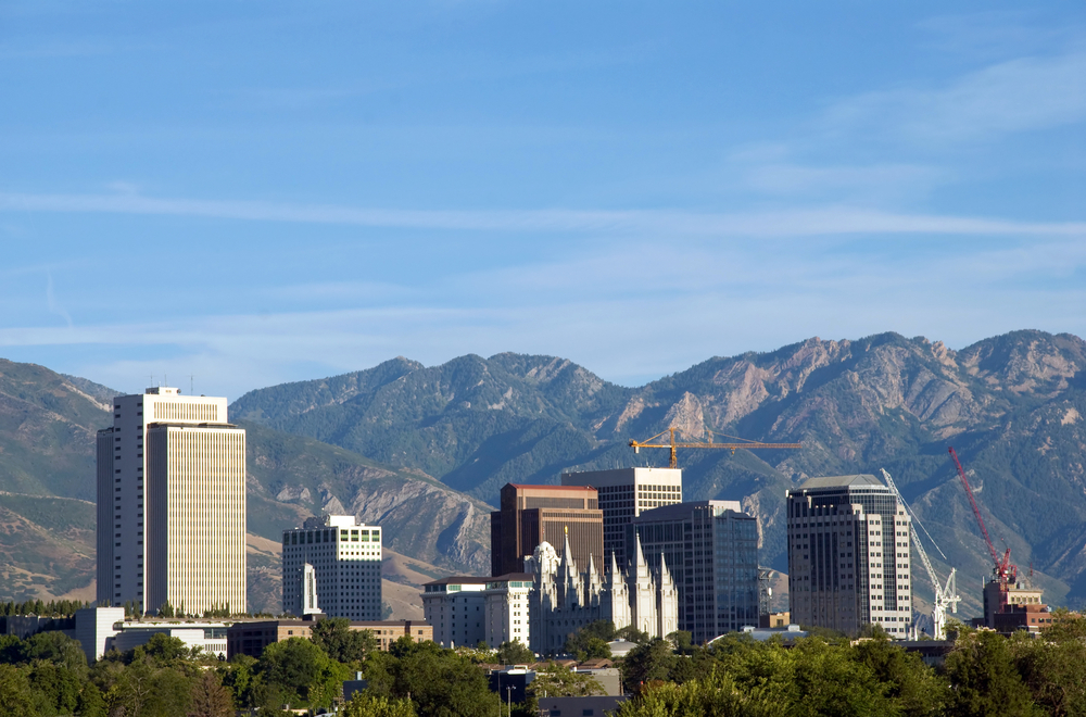 Skyline of Salt Lake City, Utah. The image shows the downtown buildings and skyline, the historic Mormon temple, and the Wasatch mountains in the background.